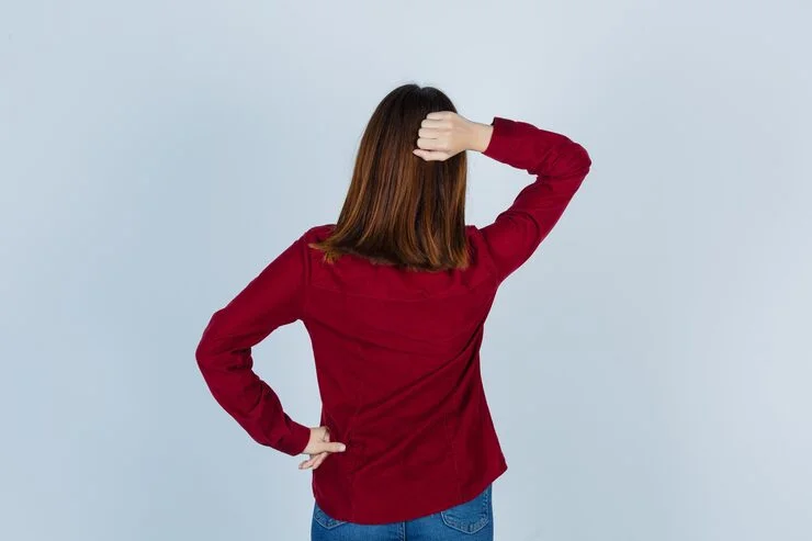 Rear view of a woman in maroon shirt placing one hand on head and the other on hip