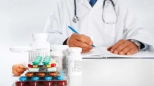 Doctor wearing white lab coat writes prescription in front of medical pills