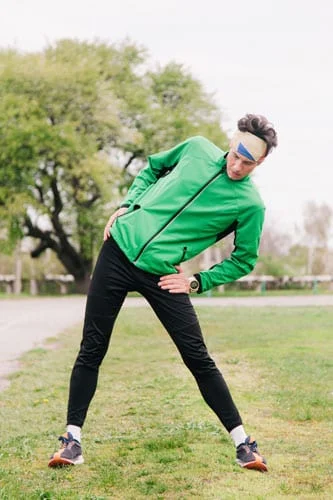 Man stretches outside wearing green top and black workout pants