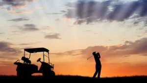 Man swings golf club beside golf cart at sunset