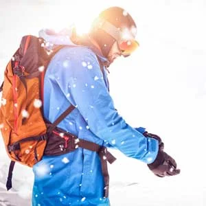 Man wearing winter ski attire and backpack holds his wrist