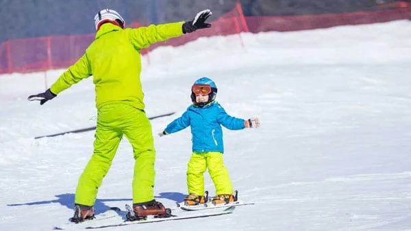 Adult and child snowboard down a hill during winter