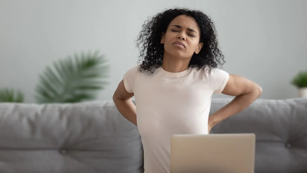 Woman sitting on couch at home experiences stiff back at being on computer