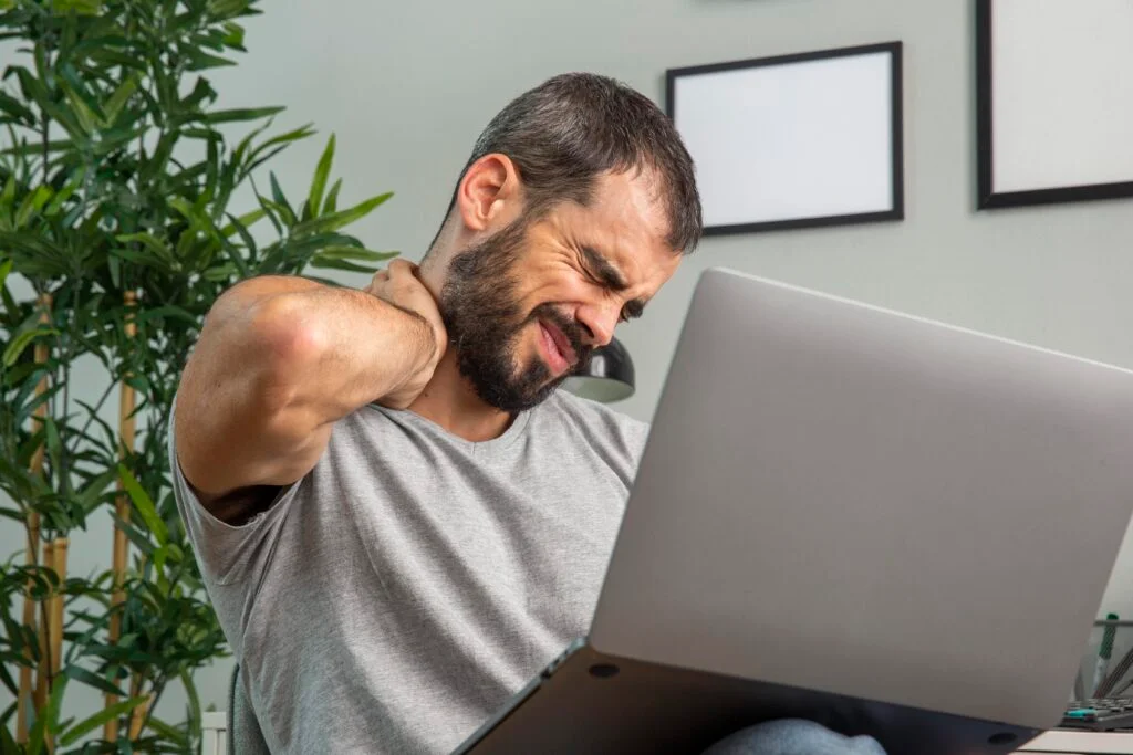 Man experiences neck pain while looking at laptop computer
