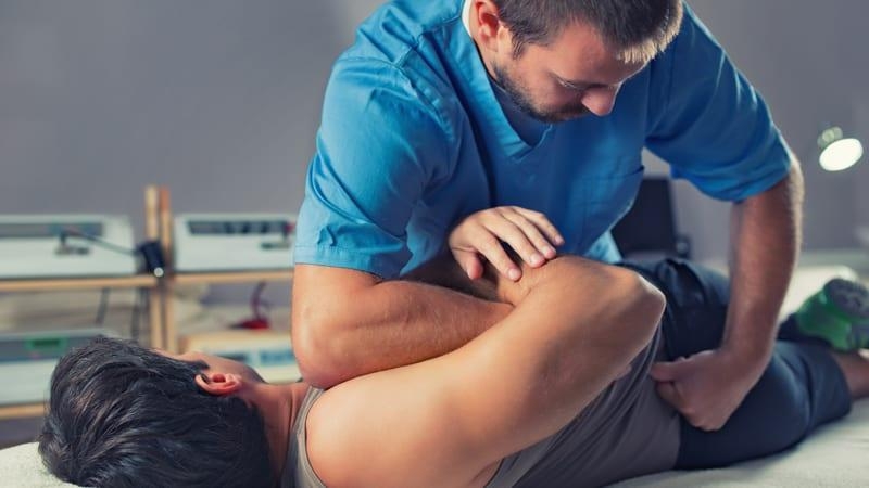 Male chiropractor adjusts lower back of male patient