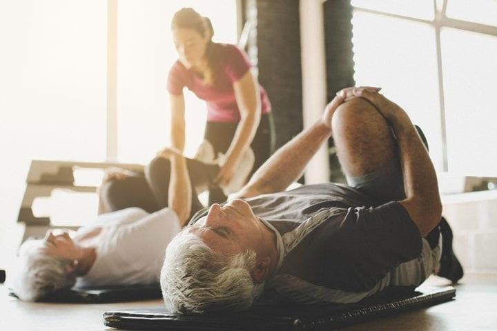 Older couples stretches on mats while therapist assists the woman