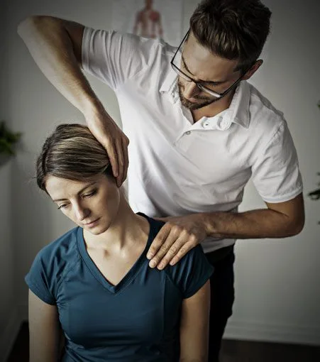 Male physical therapist adjusts female patient's neck during therapy