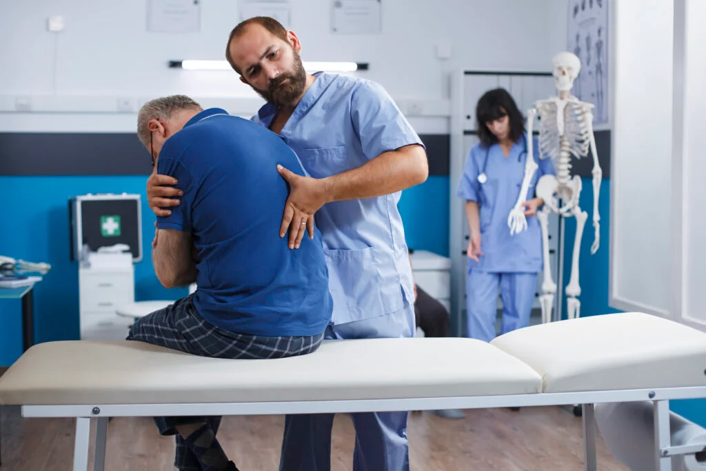 Male chiropractor adjusts back of older male patient at clinic