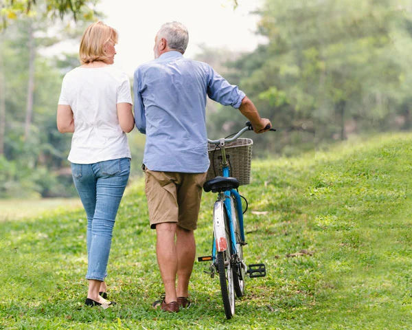 Older couple walks with bike in a park during the day