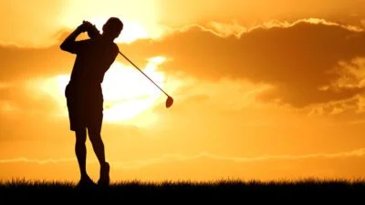 Man swings golf club at sunset