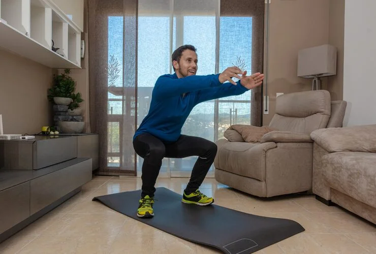 Man in workout clothes squats on mat while working out at home