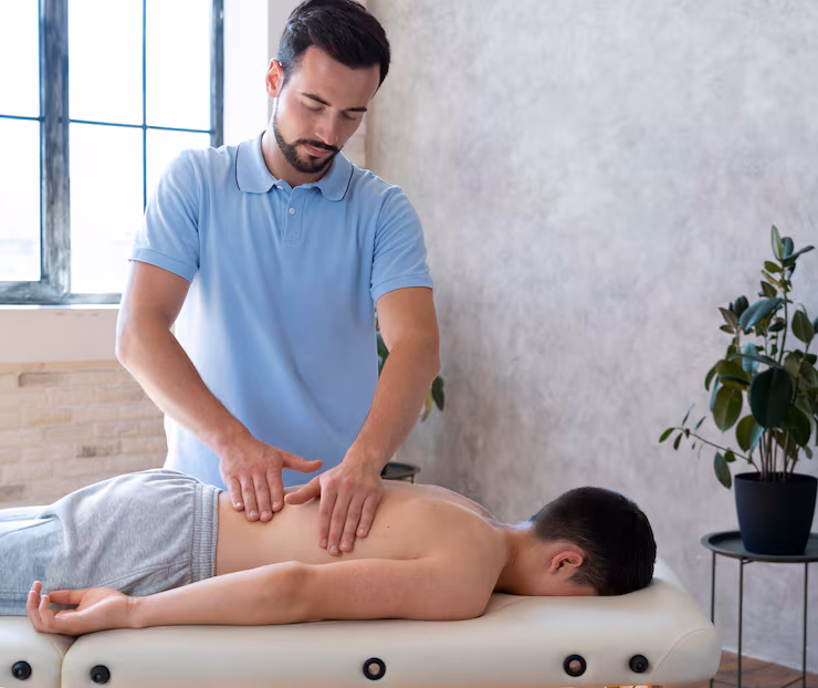 Male physical therapist massages lower back of male patient on bench at clinic