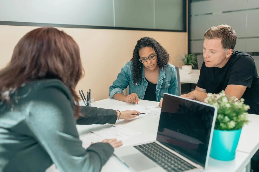 Man and two women review paperwork while seated at a desk
