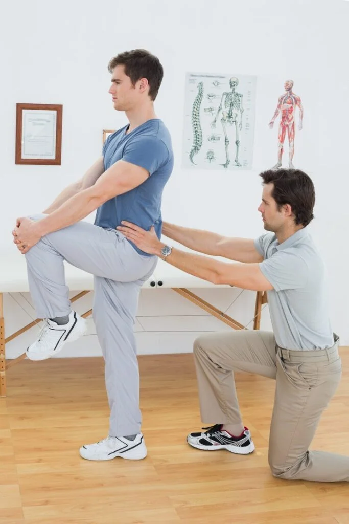 Male patient raises one leg while physical therpaist holds patient's hips